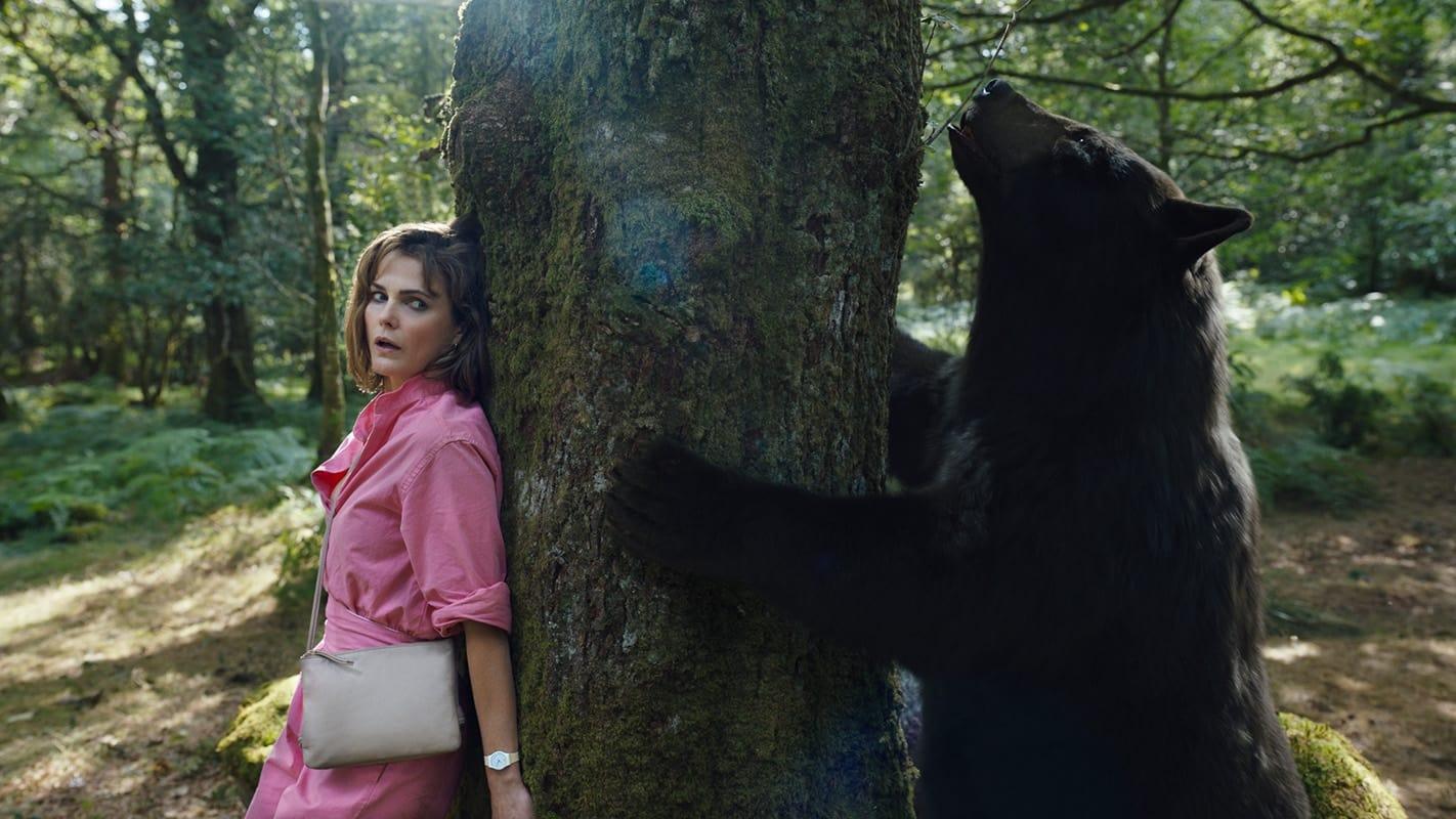Cocaine Bear star Keri Russell as Sari hiding from the titular bear behind a tree.