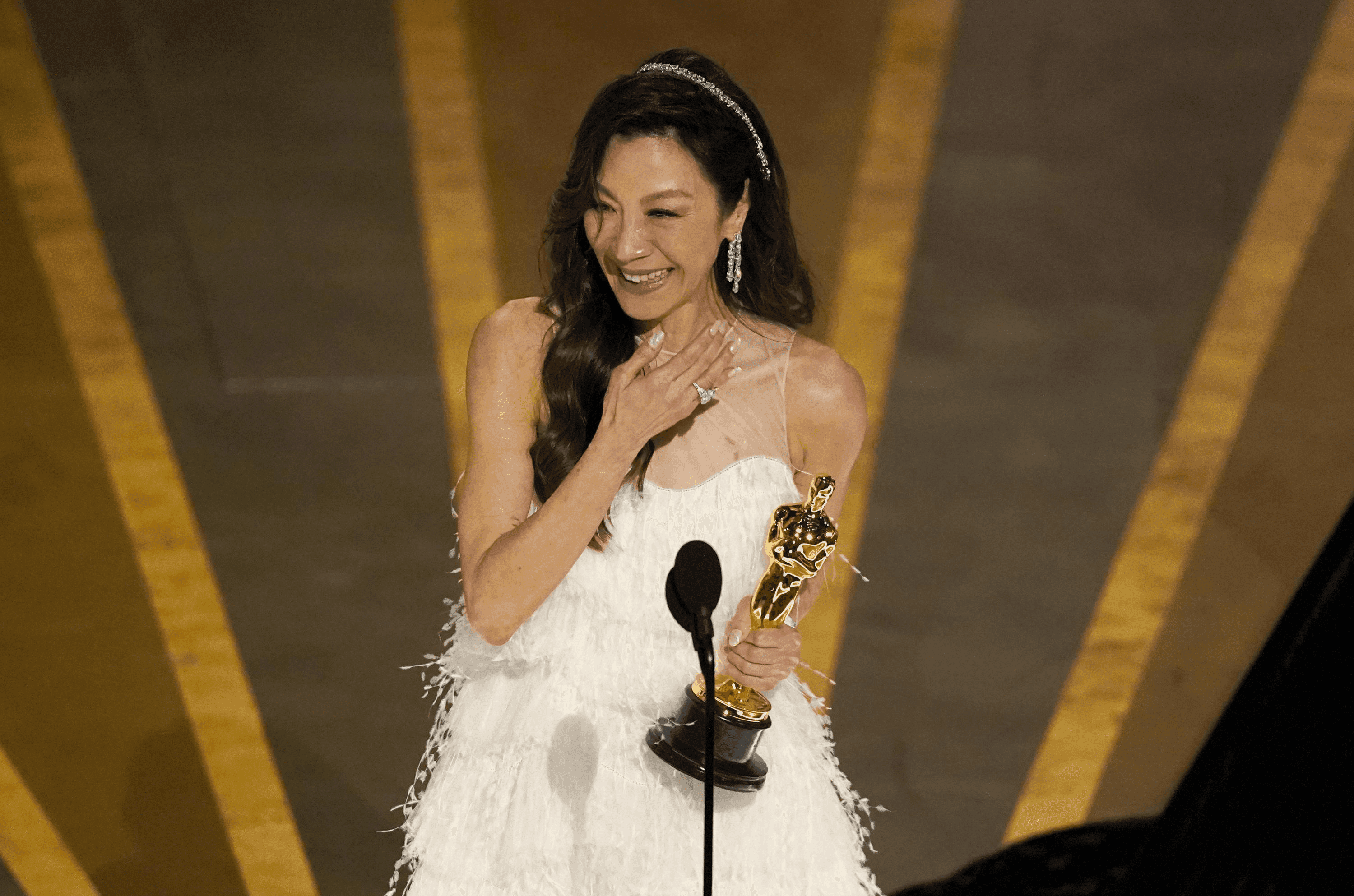 Michelle Yeoh stands in front of a microphone holding an Oscar during her acceptance speech at the 95th Academy Awards.